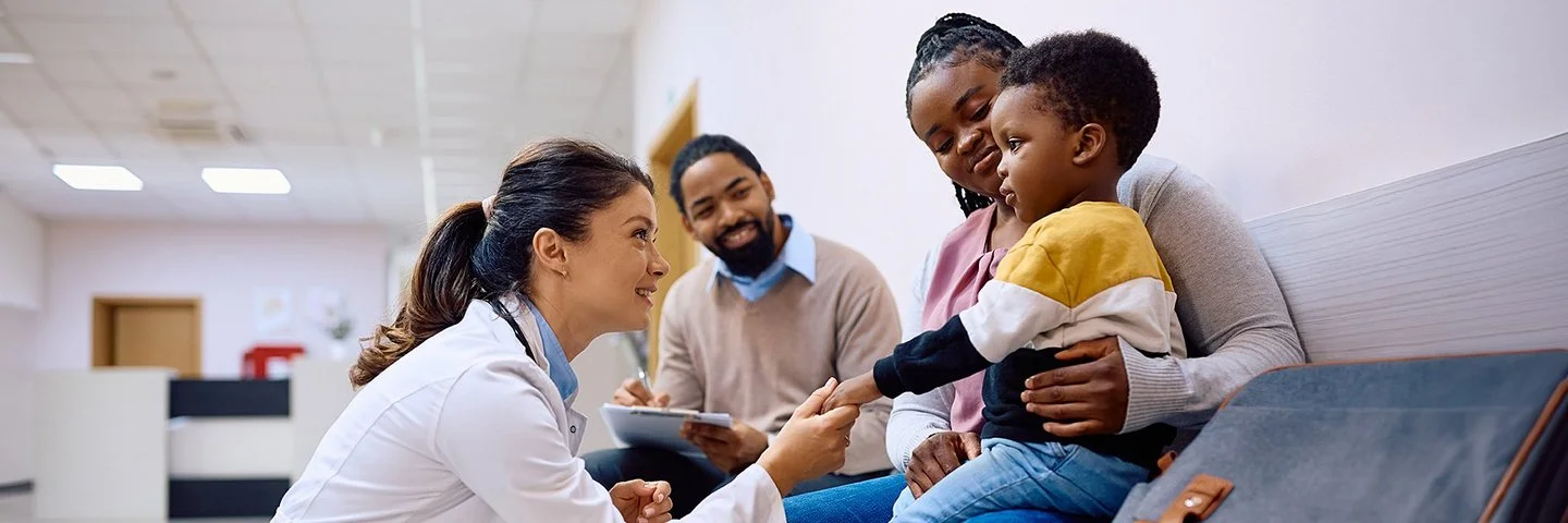 Eine junge Ärztin interagiert mit einem Kind und seiner Mutter im Warteraum einer Klinik.