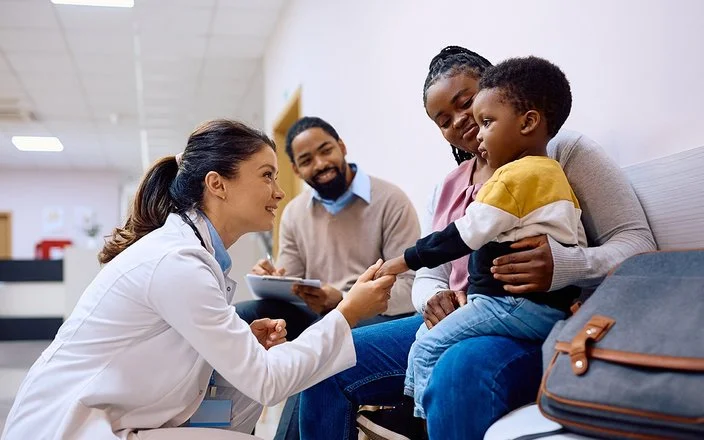 Eine junge Ärztin interagiert mit einem Kind und seiner Mutter im Warteraum einer Klinik.