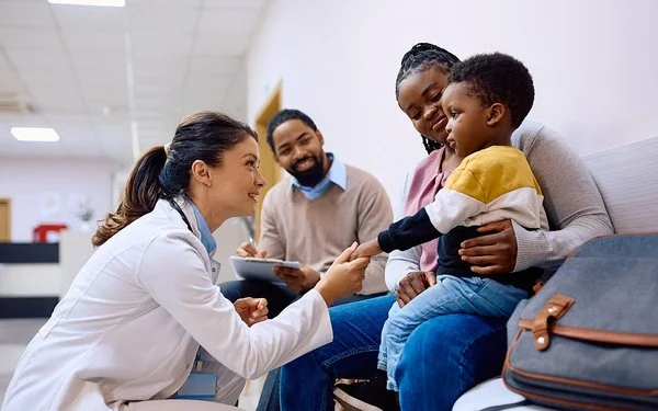 Eine junge Ärztin interagiert mit einem Kind und seiner Mutter im Warteraum einer Klinik.