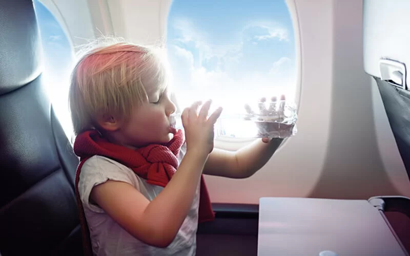 Ein kleiner Junge sitzt im Flugzeug und trinkt Wasser.