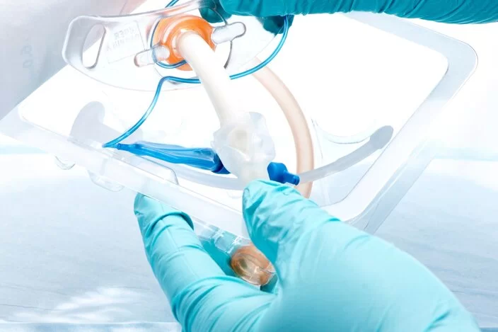 Eine Person, die medizinische Handschuhe trägt, öffnet eine steril verpackte Trachealkanüle.