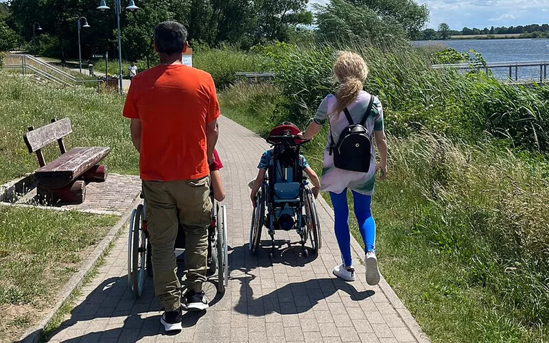 Eltern schieben die Rollstühle mit ihren schwer behinderten Kindern bei einem Ausflug im Sommer.