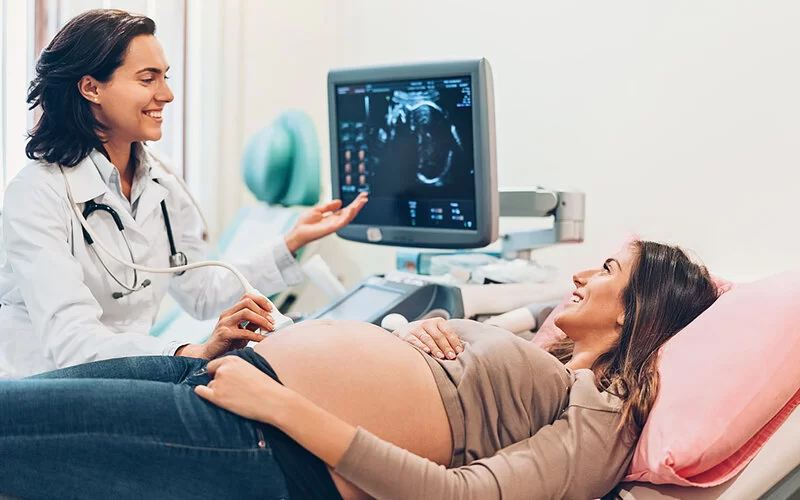Eine Ärztin führt an einer hochschwangeren Frau einen Ultraschall durch.
