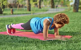 Eine junge Frau in Sportbekleidung macht sogenannte Planks auf einer Yogamatte in einem Park.