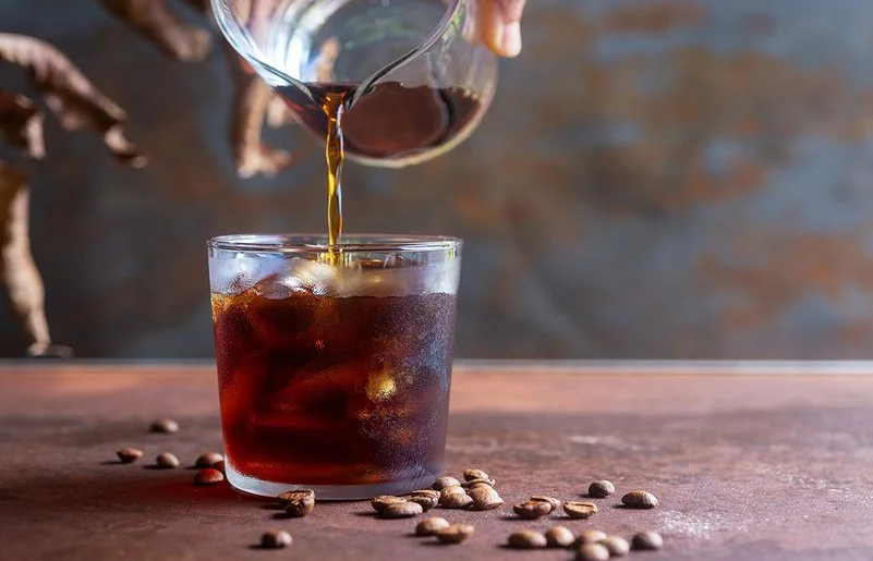Eine Person gießt Cold Brew in ein Glas mit Eiswürfeln.