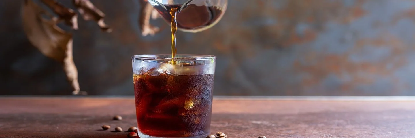 Eine Person gießt Cold Brew in ein Glas mit Eiswürfeln.