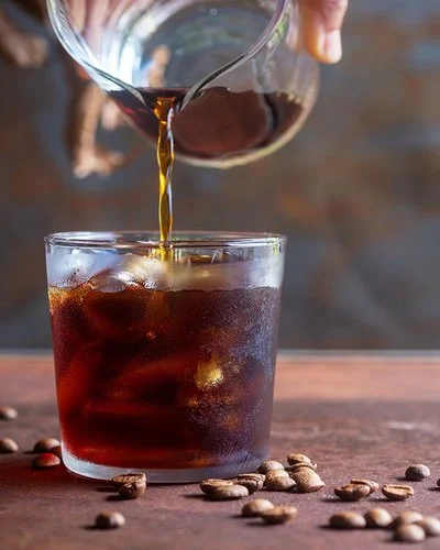 Eine Person gießt Cold Brew in ein Glas mit Eiswürfeln.