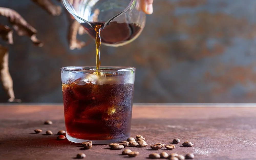 Eine Person gießt Cold Brew in ein Glas mit Eiswürfeln.