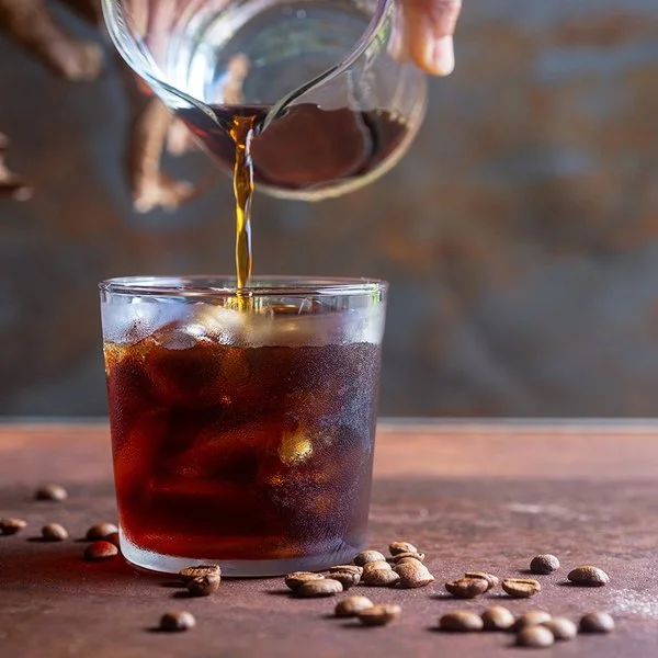 Eine Person gießt Cold Brew in ein Glas mit Eiswürfeln.
