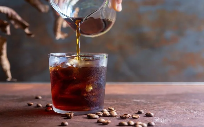Eine Person gießt Cold Brew in ein Glas mit Eiswürfeln.