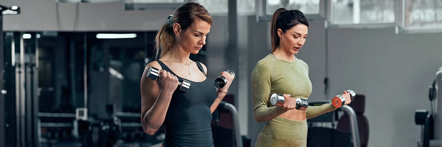 Zwei Frauen machen gemeinsam Cool-down-Übungen mit Hanteln im Fitnessstudio.