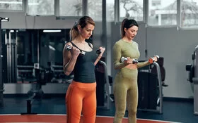 Zwei Frauen machen gemeinsam Cool-down-Übungen mit Hanteln im Fitnessstudio.