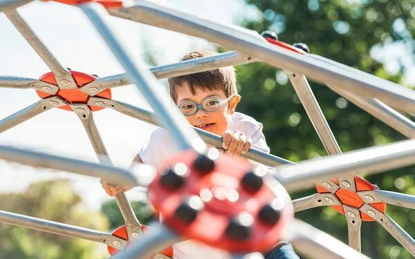 Kleiner Junge mit Trisomie 21 spielt auf einem Kletterger�üst.