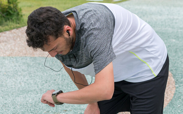 Ein Mann liest nach dem Laufen seine Pace auf seiner Fitnessarmbanduhr ab.