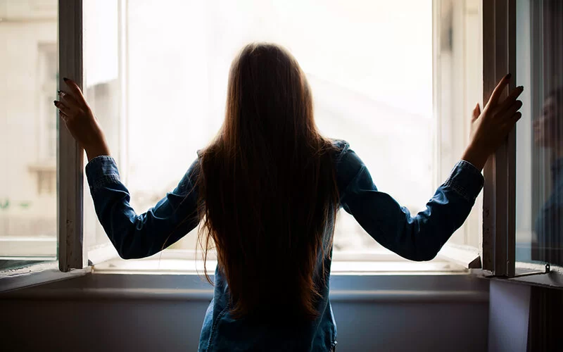 Frau steht am geöffneten Fenster, um ihre Wohnung richtig zu lüften und zu heizen.