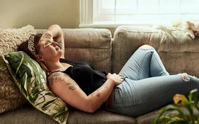 Frau liegt auf der Couch, hält sich erschöpft den Bauch und den Kopf.