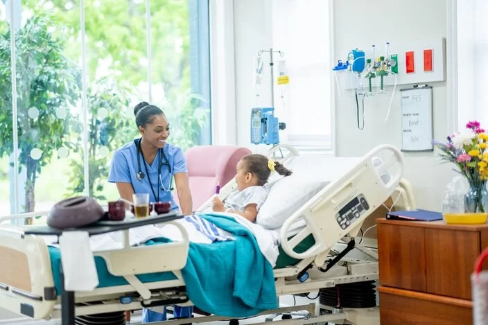 Eine Krankenschwester sitzt am Krankenbett eines Kindes. 