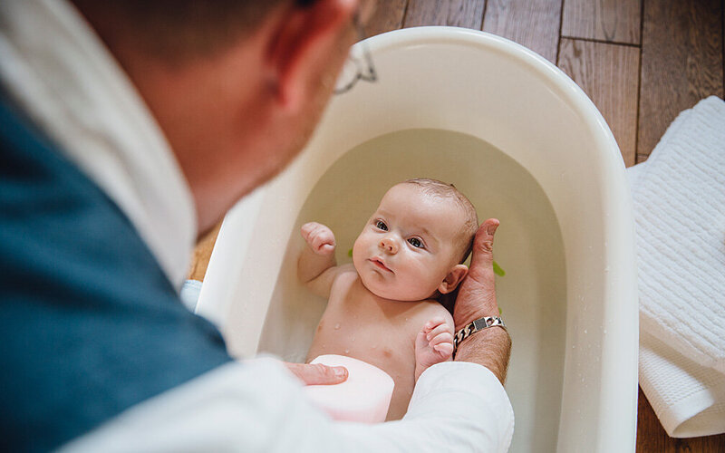 Vater badet und wäscht sein Baby in einer Wanne mit Wasser.