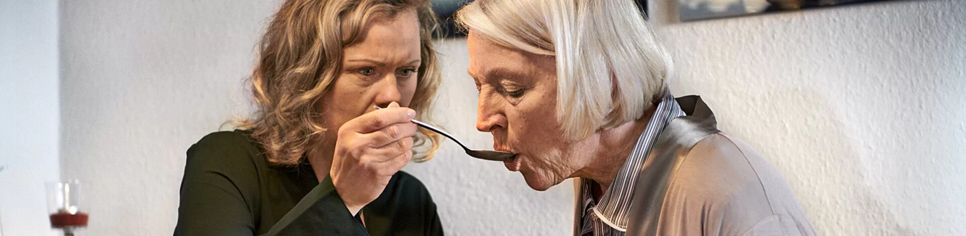Eine pflegende Angehörige füttert eine pflegebedürftige ältere Frau. Sie kann ab Pflegegrad 2 Entlastungsleistungen wie etwa die Kurzzeitpflege beanspruchen.