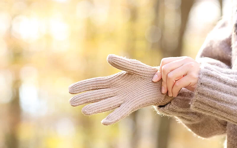 Gegen kalte Hände: Eine Frau zieht eine dicken Strickhandschuh über ihre rechte Hand.
