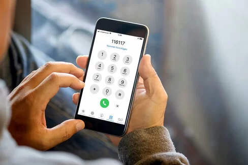 Mann hält Smartphone in der Hand und wählt 116 117.