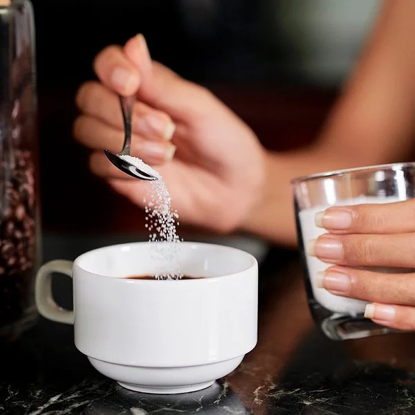 Eine Frau gibt mit einem kleinen Löffel Sorbit in eine Tasse Kaffee.