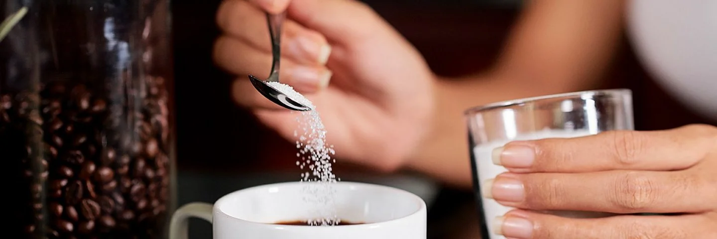 Eine Frau gibt mit einem kleinen Löffel Sorbit in eine Tasse Kaffee.