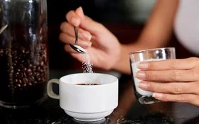 Eine Frau gibt mit einem kleinen Löffel Sorbit in eine Tasse Kaffee.