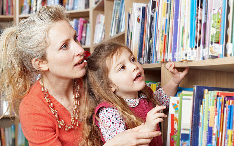 Frau hat eine Kinderpatenschaft für ein junges Mädchen inne, zusammen sind sie in der Bücherei.