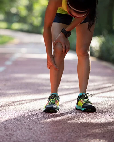 Eine junge Frau in Sportkleidung hält sich vor Schmerzen die Wade.