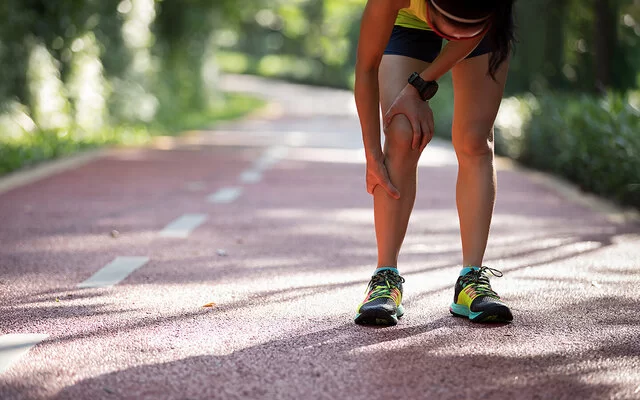 Eine junge Frau in Sportkleidung hält sich vor Schmerzen die Wade.