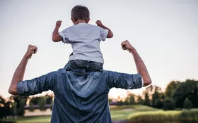 Vater trägt Sohn auf den Schultern und stärkt das Selbstbewusstsein des Kindes.
