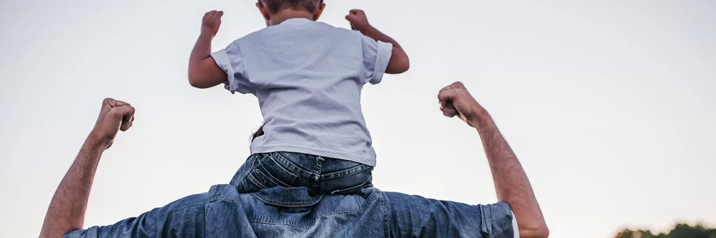 Vater trägt Sohn auf den Schultern und stärkt das Selbstbewusstsein des Kindes.