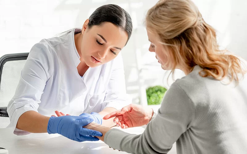 Eine junge Hautärztin untersucht den Unterarm einer Patientin.