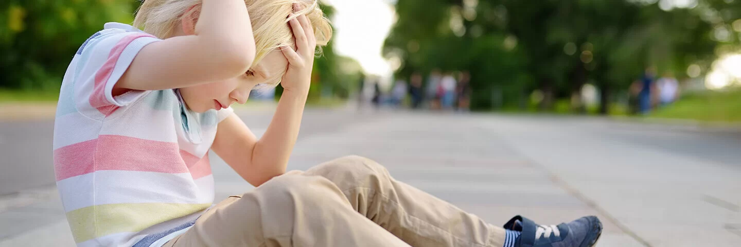 Kleiner Junge sitzt auf dem Boden und hält sich den Kopf. Er hat vielleicht eine Gehirnerschütterung.