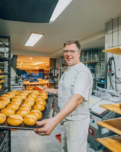 Der Bäckermeister Stefan Steeg schiebt in seiner Backstube ein großes Blech mit frisch gebackenen Brötchen in ein Backwarenregal.