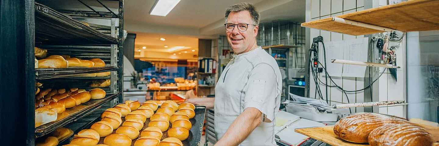 Der Bäckermeister Stefan Steeg schiebt in seiner Backstube ein großes Blech mit frisch gebackenen Brötchen in ein Backwarenregal.