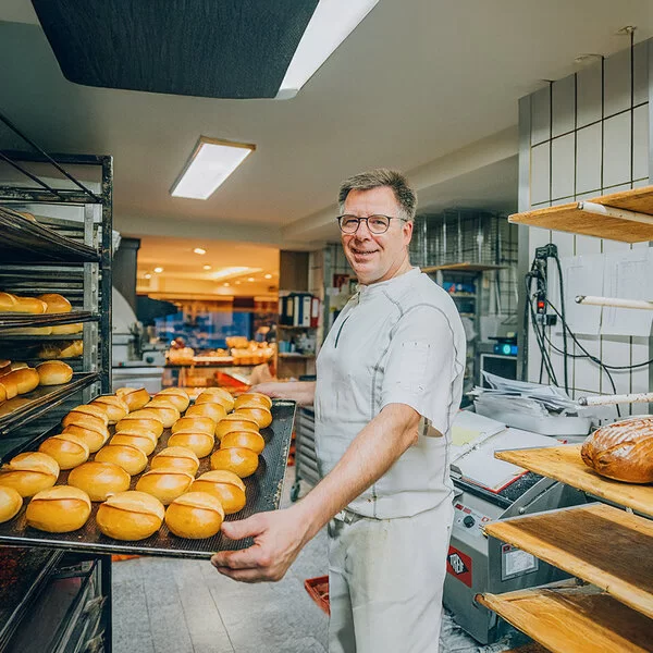 Der Bäckermeister Stefan Steeg schiebt in seiner Backstube ein großes Blech mit frisch gebackenen Brötchen in ein Backwarenregal.
