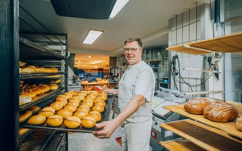 Der Bäckermeister Stefan Steeg schiebt in seiner Backstube ein großes Blech mit frisch gebackenen Brötchen in ein Backwarenregal.