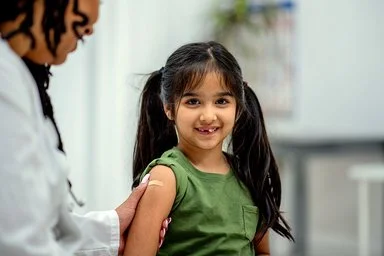 Eine Ärztin klebt einem Mädchen im Grundschulalter nach der Impfung ein Pflaster auf den Oberarm.