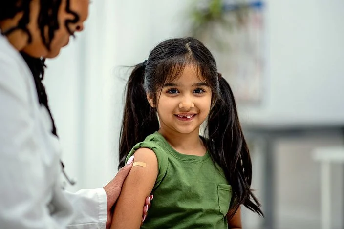 Eine Ärztin klebt einem Mädchen im Grundschulalter nach der Impfung ein Pflaster auf den Oberarm.