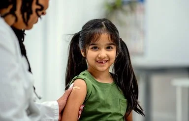 Eine Ärztin klebt einem Mädchen im Grundschulalter nach der Impfung ein Pflaster auf den Oberarm.