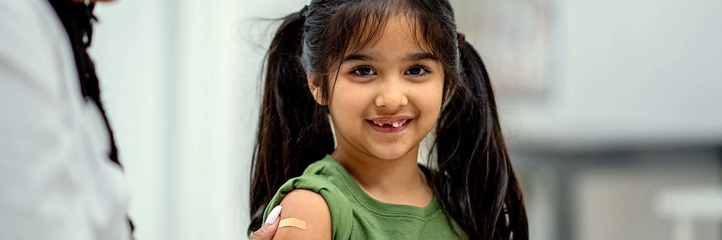 Eine Ärztin klebt einem Mädchen im Grundschulalter nach der Impfung ein Pflaster auf den Oberarm.