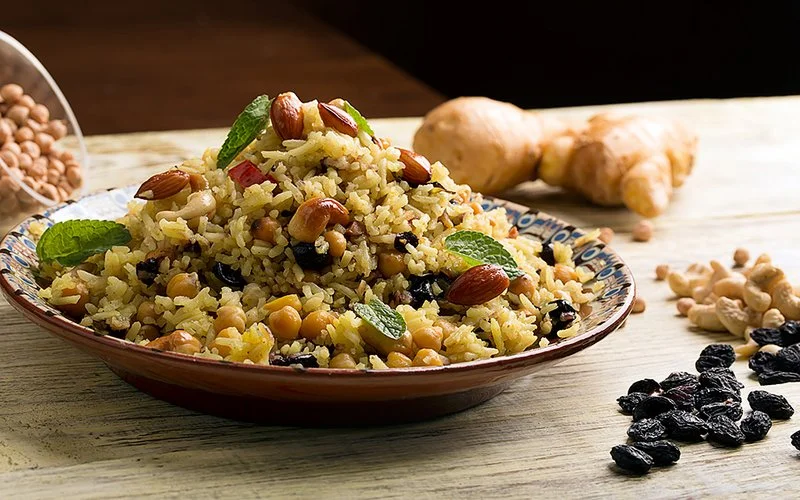 Auf einem Teller ist ein traditionelles Gericht aus Fernost mit Reis, Kirchererbsen, Rosinen und Minze angerichtet.