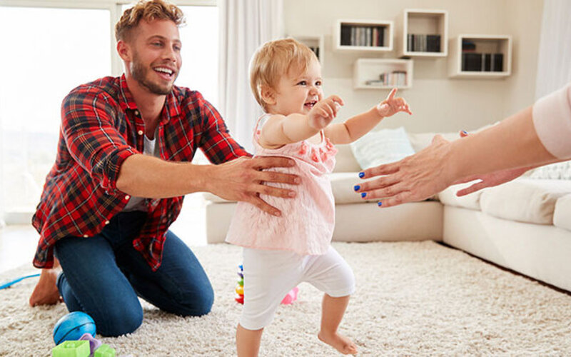 Vater und Mutter bringen ihrem Baby spielend das Laufen bei, es ist eine wichtige Phase in der Entwicklung eines Babys.