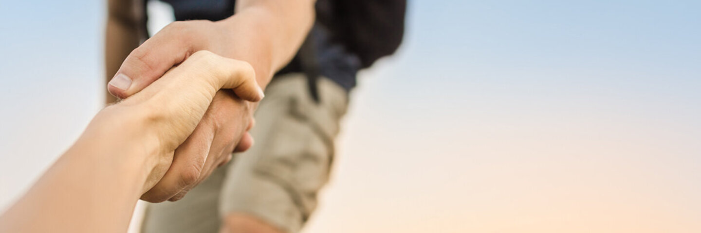 Ein Wanderer reicht einem anderen die Hand, um ihm beim Aufstieg zu helfen