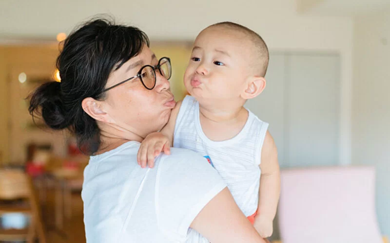 Mutter hält Kind auf dem Arm und kommuniziert in Babysprache.