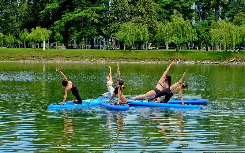 Fünf Frauen machen auf einem See SUP-Yoga auf ihren Boards.