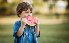 Kleines Mädchen im Jeanskleid isst ein Stück gesunde Wassermelone.