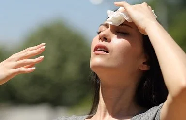 Eine Frau steht bei Sonnenschein im Freien. Sie kühlt ihre Stirn mit einem Tuch und fächelt sich Luft zu.